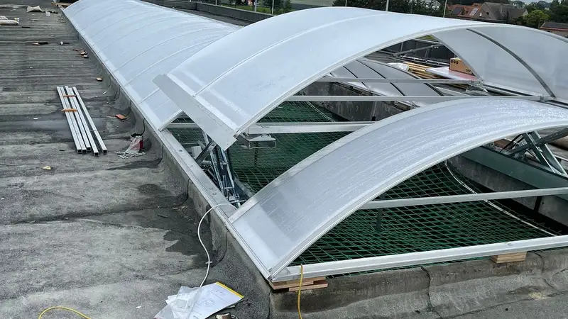 Gebogen lichtstraten van doorschijnend kunststof op een plat dak, met een groen net eronder