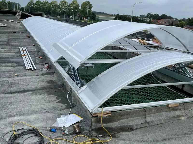 Gebogen lichtstraten van doorschijnend kunststof op een plat dak, met een groen net eronder