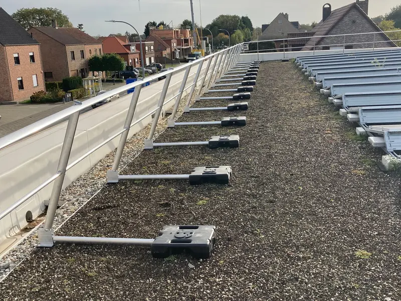 Vrijstaande aluminium leuning met betonvoeten langs de rand van een plat dak met zonnepanelen