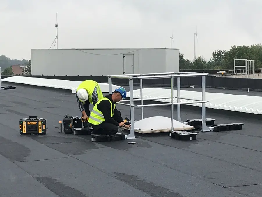 Twee werkers plaatsen een aluminium leuning rond een lichtkoepel op een plat dak