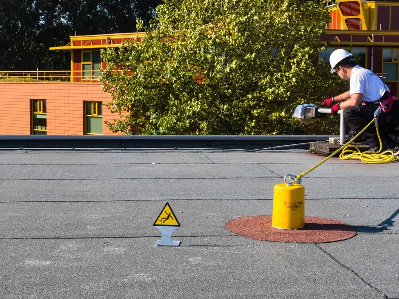 Geel ankerpunt op een rode schijf op een plat dak, met een lijn naar een werker in harnas