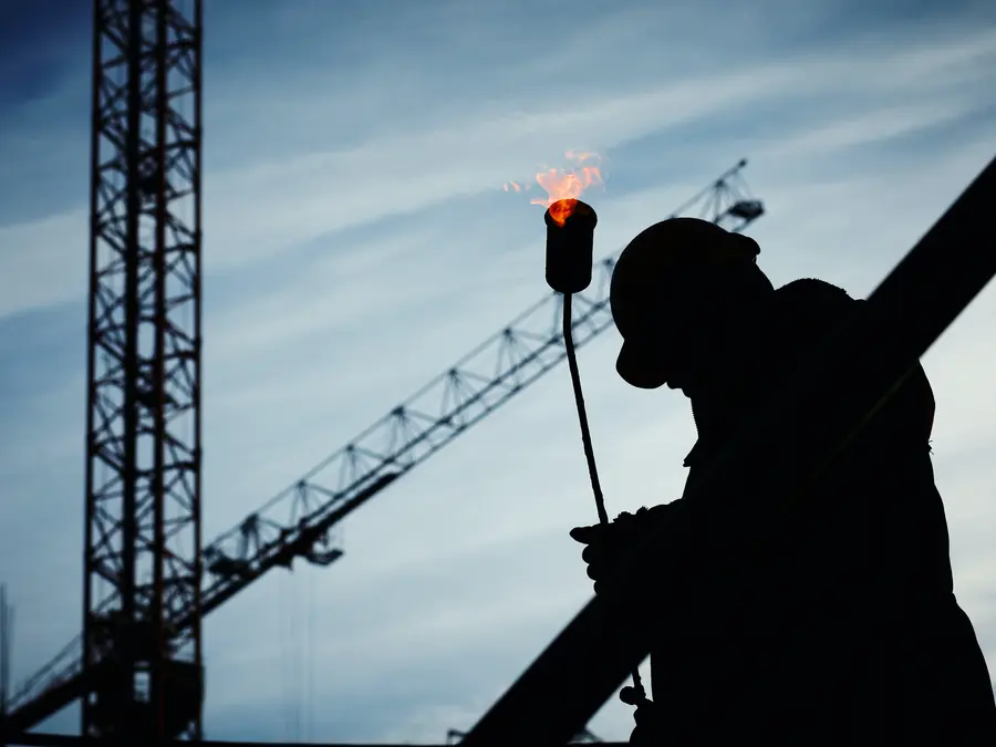Silhouet van een dakwerker met een brander, met bouwkranen op de achtergrond