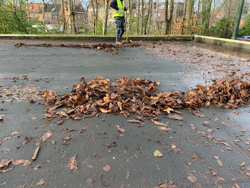 Medewerker in een fluohesje veegt bladeren samen op een plat dak.