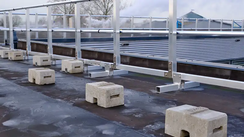 Aluminium borstwering op betonnen voeten langs de rand van een plat dak