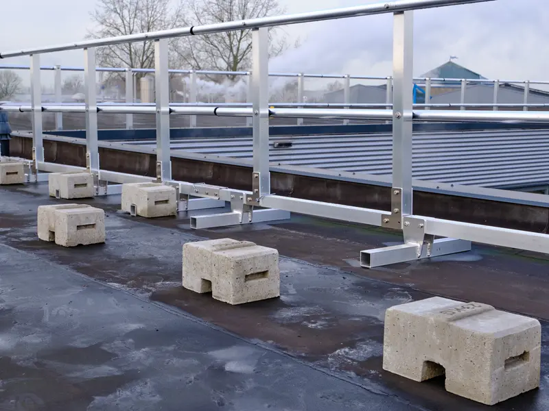Aluminium borstwering op betonnen voeten langs de rand van een plat dak