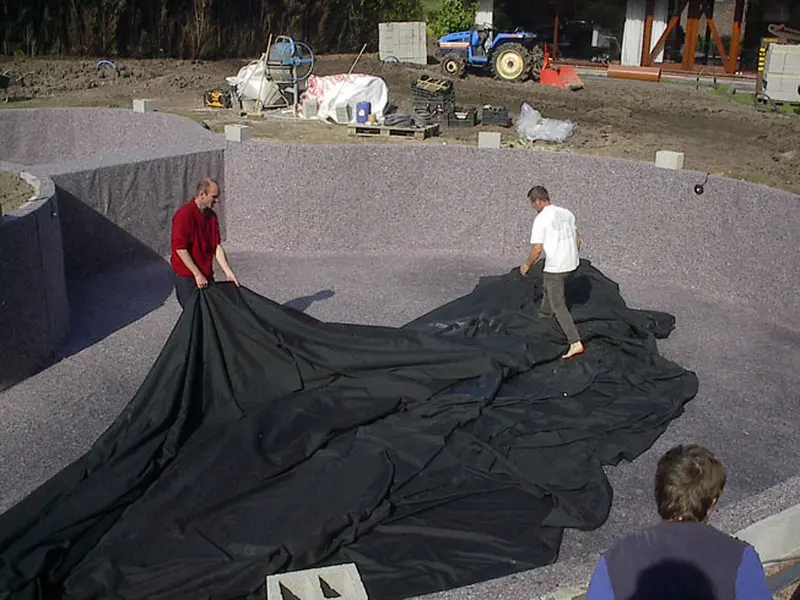 Twee mannen leggen een zwarte EPDM-folie uit één stuk in een vijver